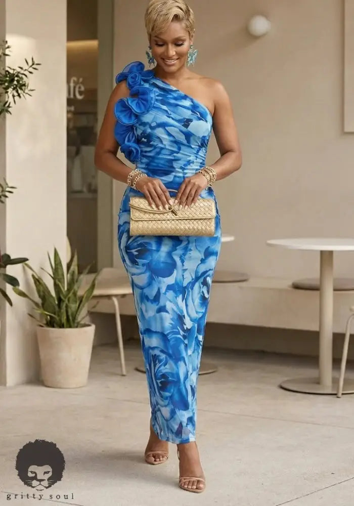 Woman in a blue floral dress holding a beige clutch in an indoor setting.